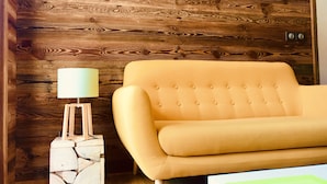 A room with a wooden wall, a yellow sofa, and a lamp on a wooden stand. - IN NEED OF FRESH AIR, NATURE AND CALM? (Molines-en-Queyras)