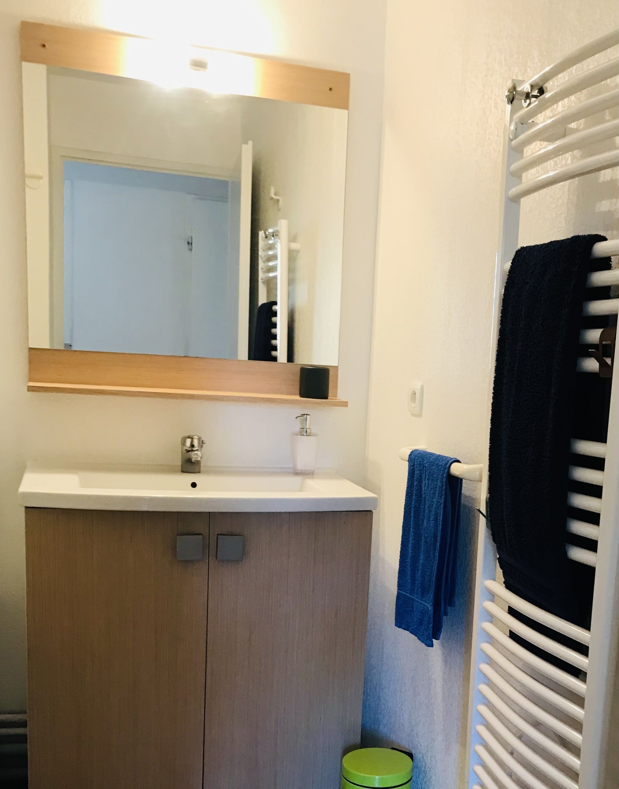 Ein Badezimmer mit Holzschrank, Waschbecken, Spiegel und Handtuchhalter mit schwarzem Handtuch.