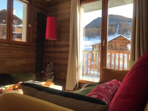 Una habitación acogedora con detalles de madera, un ventanal con vistas a una montaña nevada y una lámpara roja.