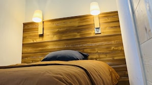 A bedroom with a wooden headboard, two wall-mounted lights, and a bed with a brown cover. - IN NEED OF FRESH AIR, NATURE AND CALM? (Molines-en-Queyras)
