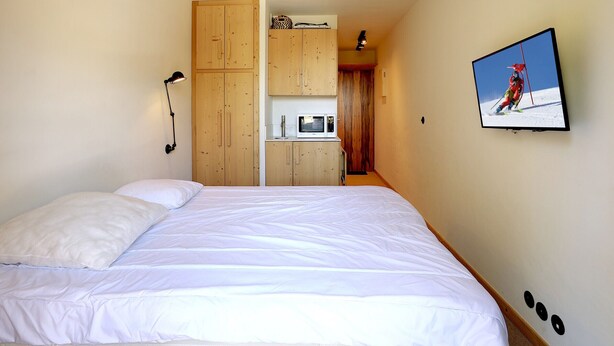 A bedroom with a bed, wooden wardrobe, a microwave, and a television on the wall. - Charming mini-studio in Courchevel 1850 with parking (Courchevel 1850)