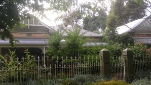 Un jardín con cerca metálica, distintas plantas y un edificio de techo tradicional.