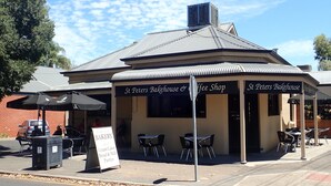 Una panadería y cafetería con terraza y un letrero que anuncia pasteles de crema, pan y repostería.