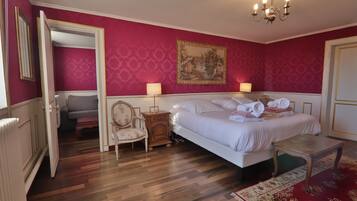 A hotel room with a bed, a chair, a nightstand, a painting, and a chandelier.