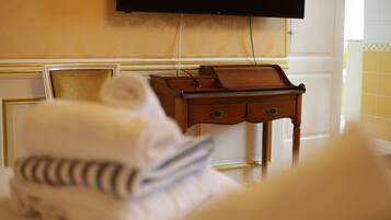 Una habitación de hotel con cama, mesita de noche de madera, televisión montada en la pared y ventana con paredes de azulejos amarillos.
