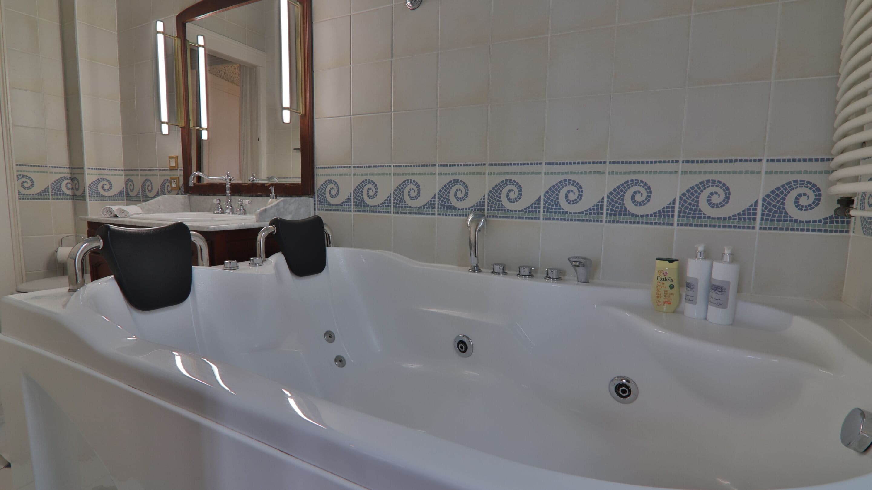 Une salle de bain avec une grande baignoire, un miroir, un lavabo et un porte-serviettes.