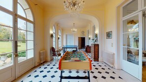Un pasillo amplio con una mesa de fútbol de mesa, ventanas grandes y un candelabro.