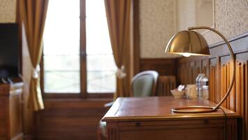 A wooden desk with a lamp, a chair, and a window with curtains.