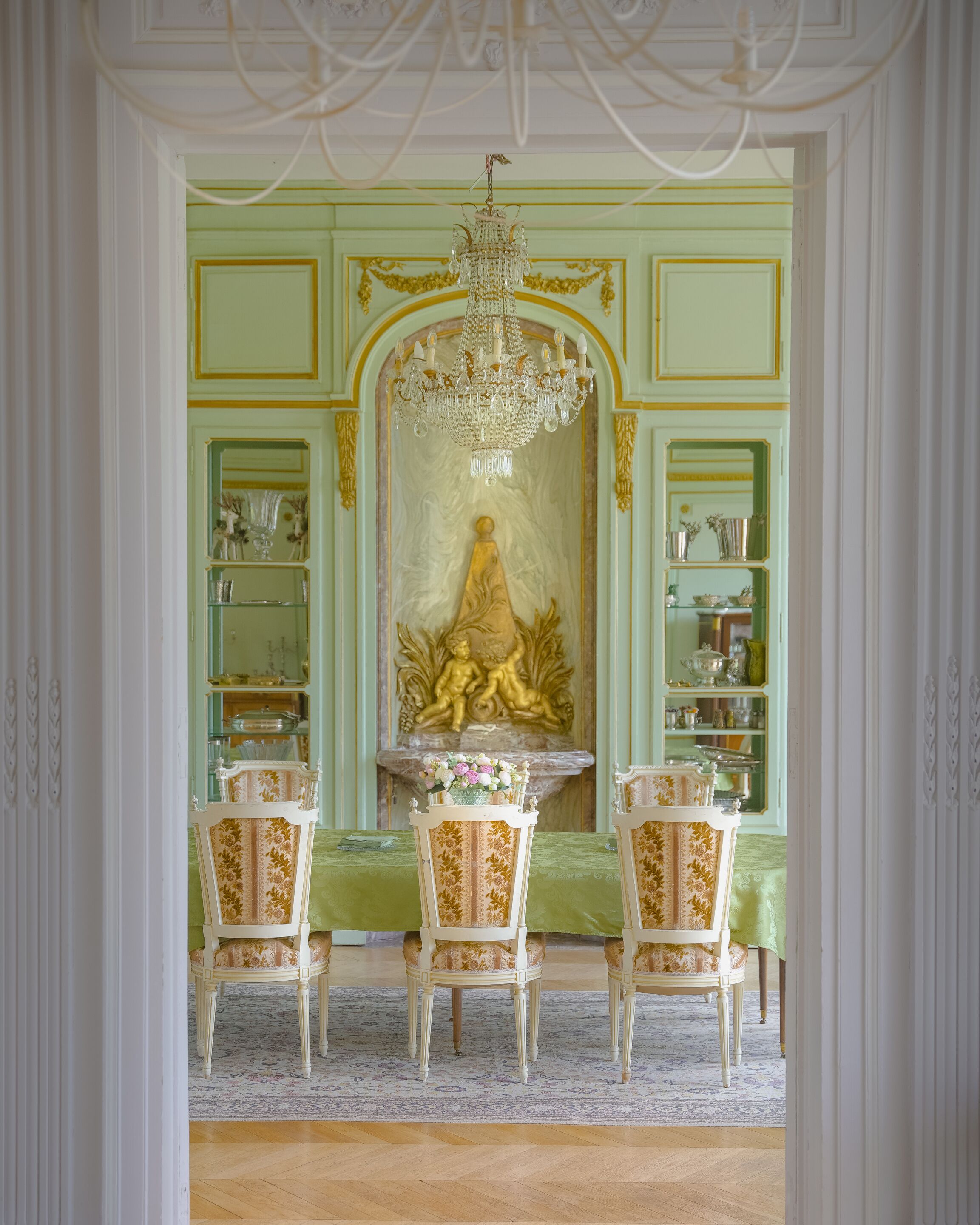 Ein Raum mit einem Chandelier, einer Statue und einer grünen Wand mit Regalen.
