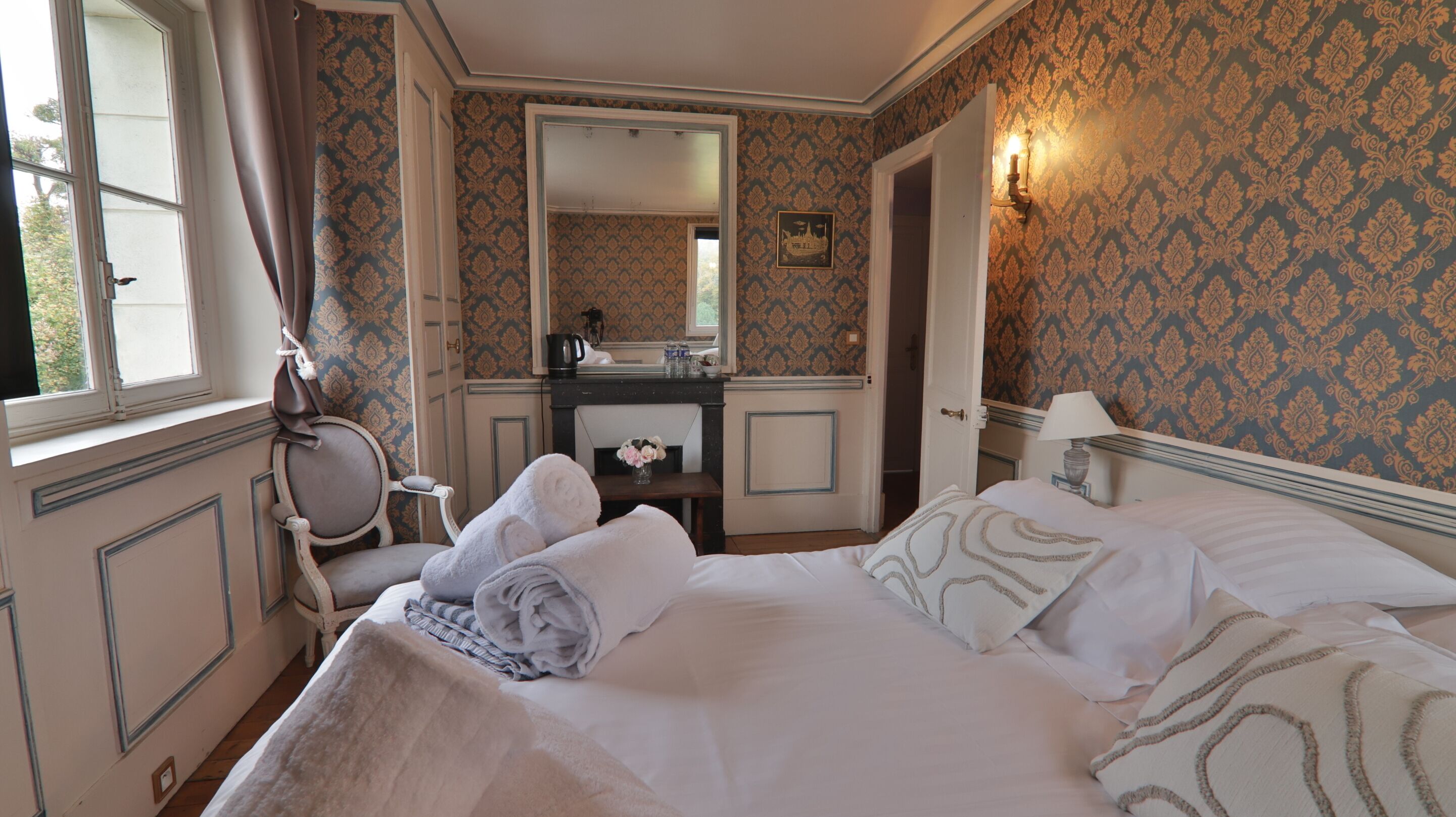 A hotel room with a bed, a chair, a desk with a mirror, and a window.