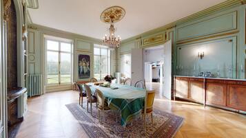 A dining room with a table set for four, a chandelier, and a view through large windows.