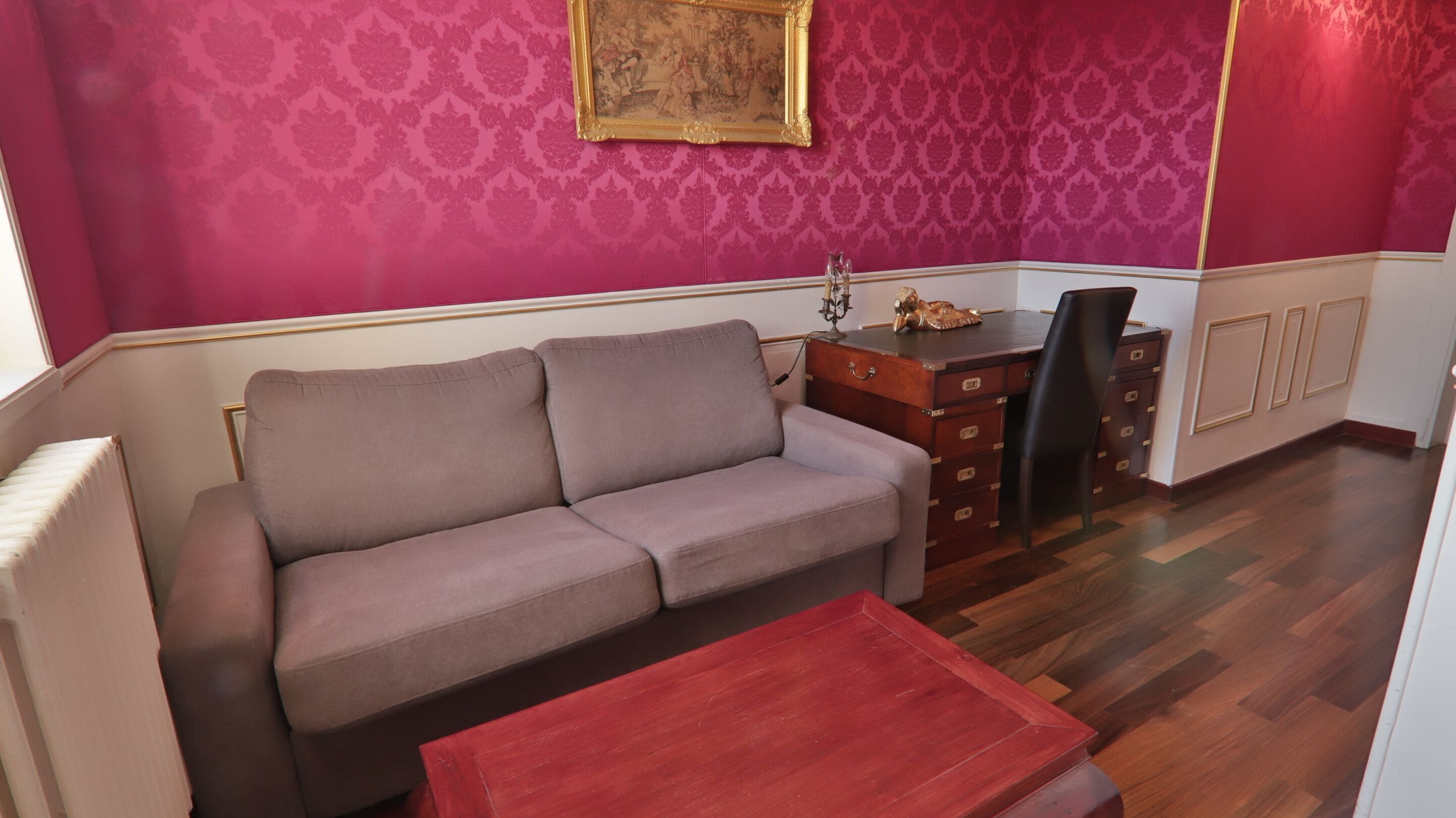 Una habitación con sofá, un escritorio de madera, una silla y una mesa roja.