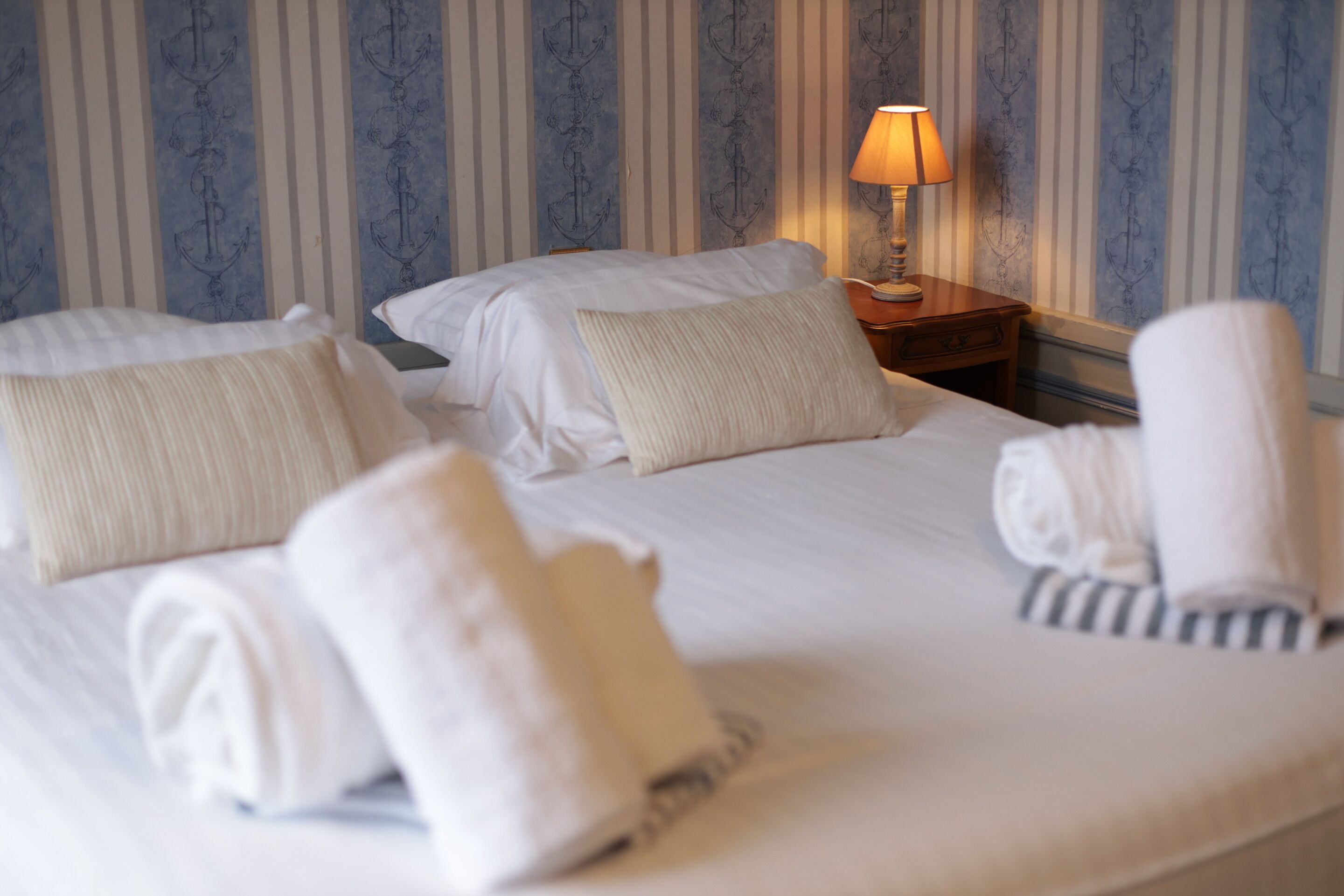 Une chambre d’hôtel avec un lit, des oreillers, une table de chevet avec une lampe et des serviettes.