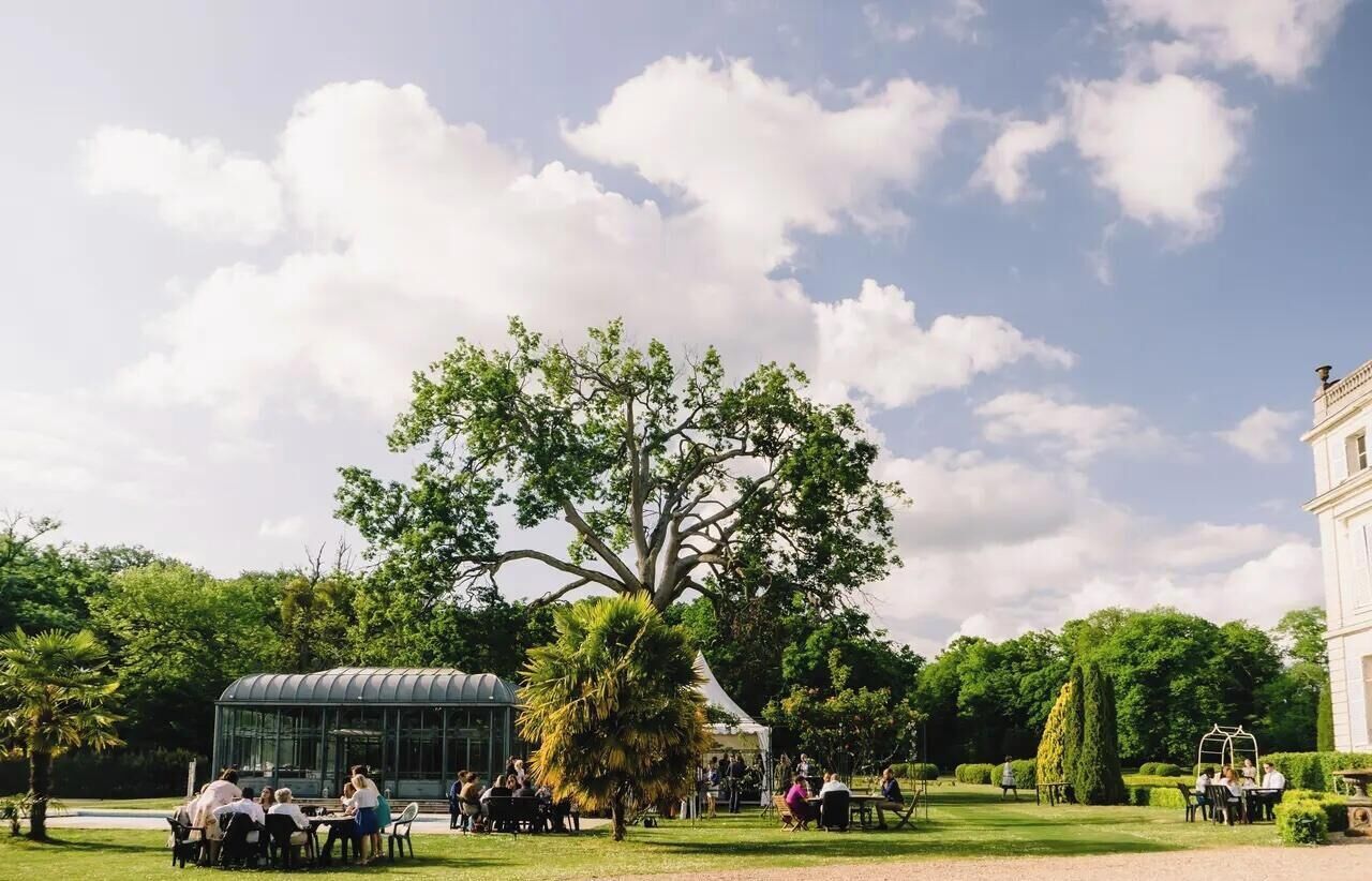 Un jardín con mesas y sillas, un árbol grande y un edificio al fondo.