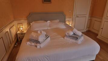A neatly made bed with pillows and folded towels, a bedside lamp, and a wardrobe in a hotel room.