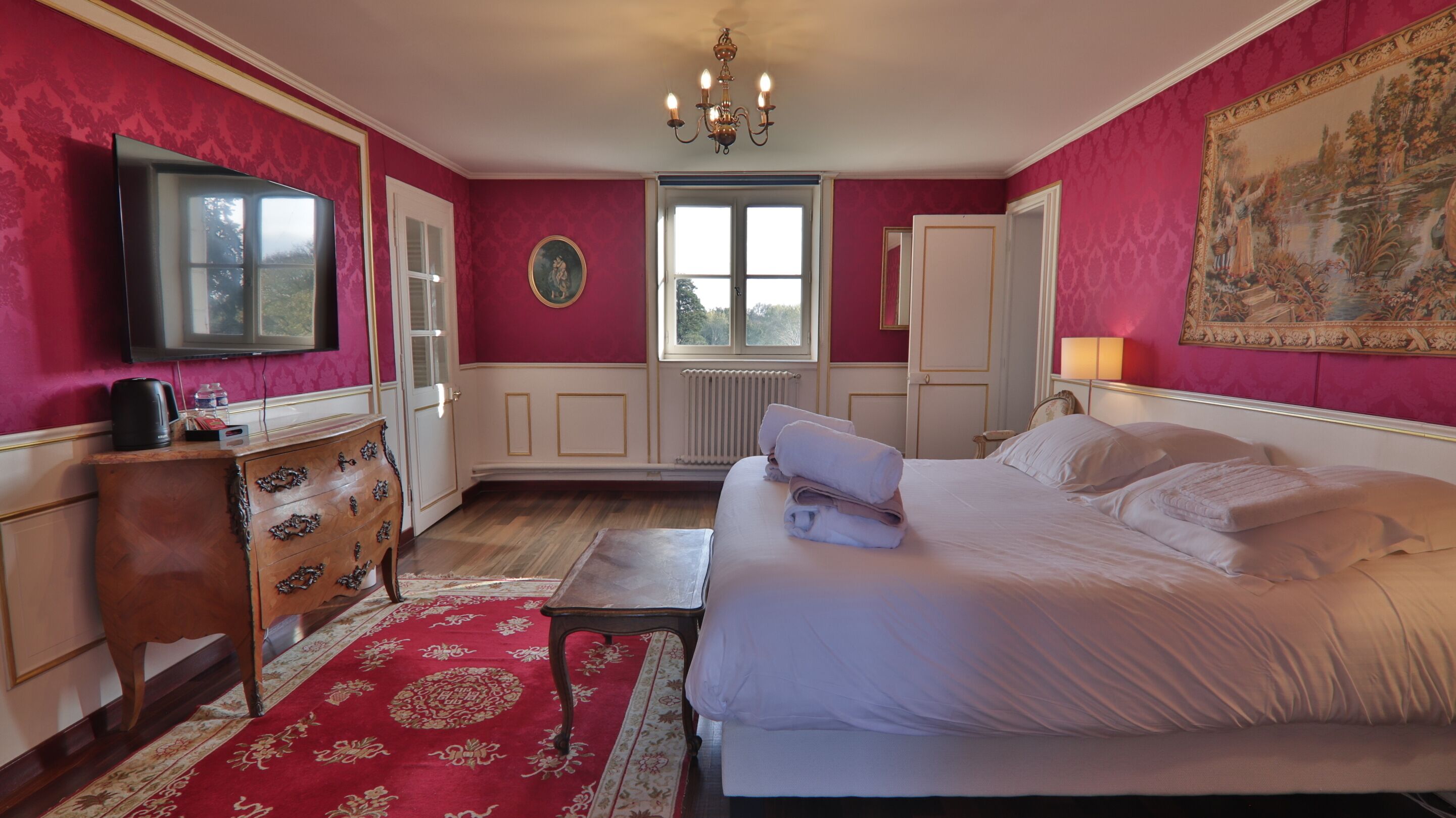 A bedroom with a bed, a dresser, a television, a window, and a painting on the wall.