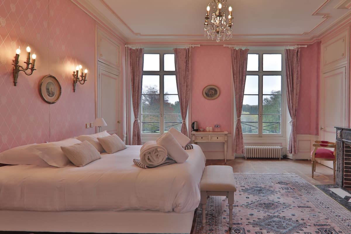 A bedroom with a large bed, a desk, a radiator, and a fireplace.