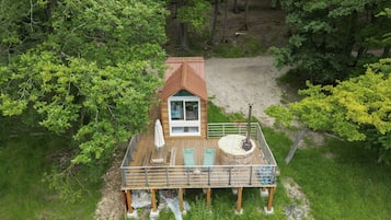 A wooden cabin with a deck, a hot tub, and a view of the surrounding forest.