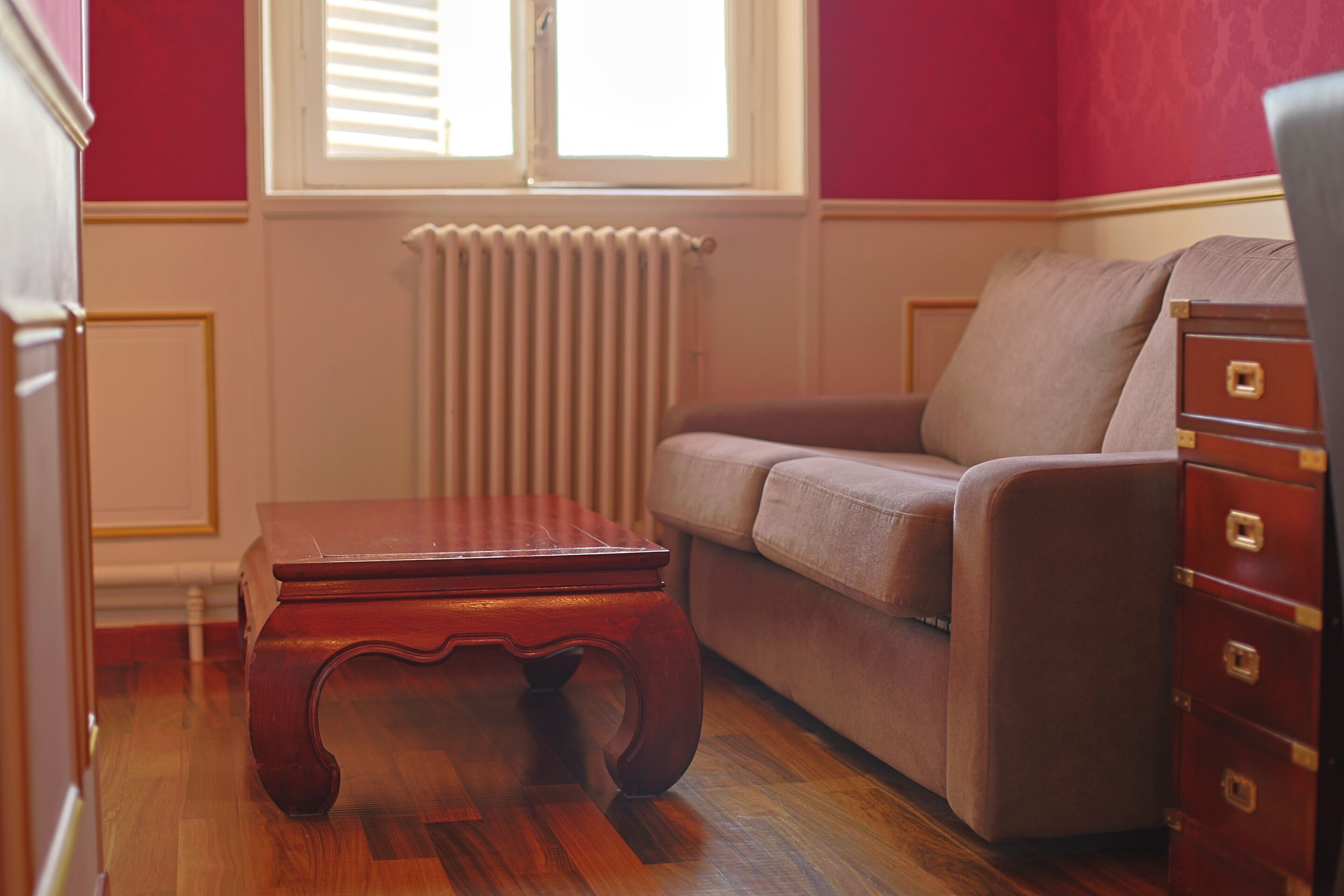 A room with a wooden coffee table, a sofa, a dresser, and a radiator.
