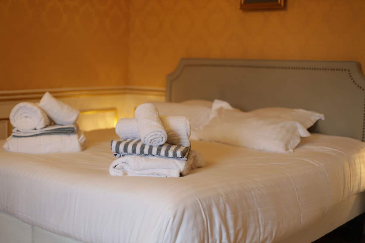A neatly made bed with rolled towels and pillows, a headboard, and a wall with a framed picture.