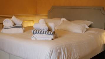 A neatly made bed with rolled towels and pillows, a headboard, and a wall with a framed picture.