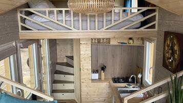 A compact cabin with a loft bedroom, a kitchenette, and a dining area.