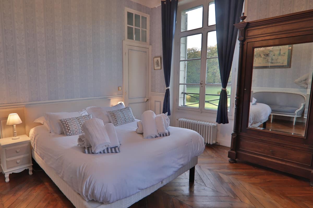 A bedroom with a large bed, a nightstand, a dresser, and a window with curtains.