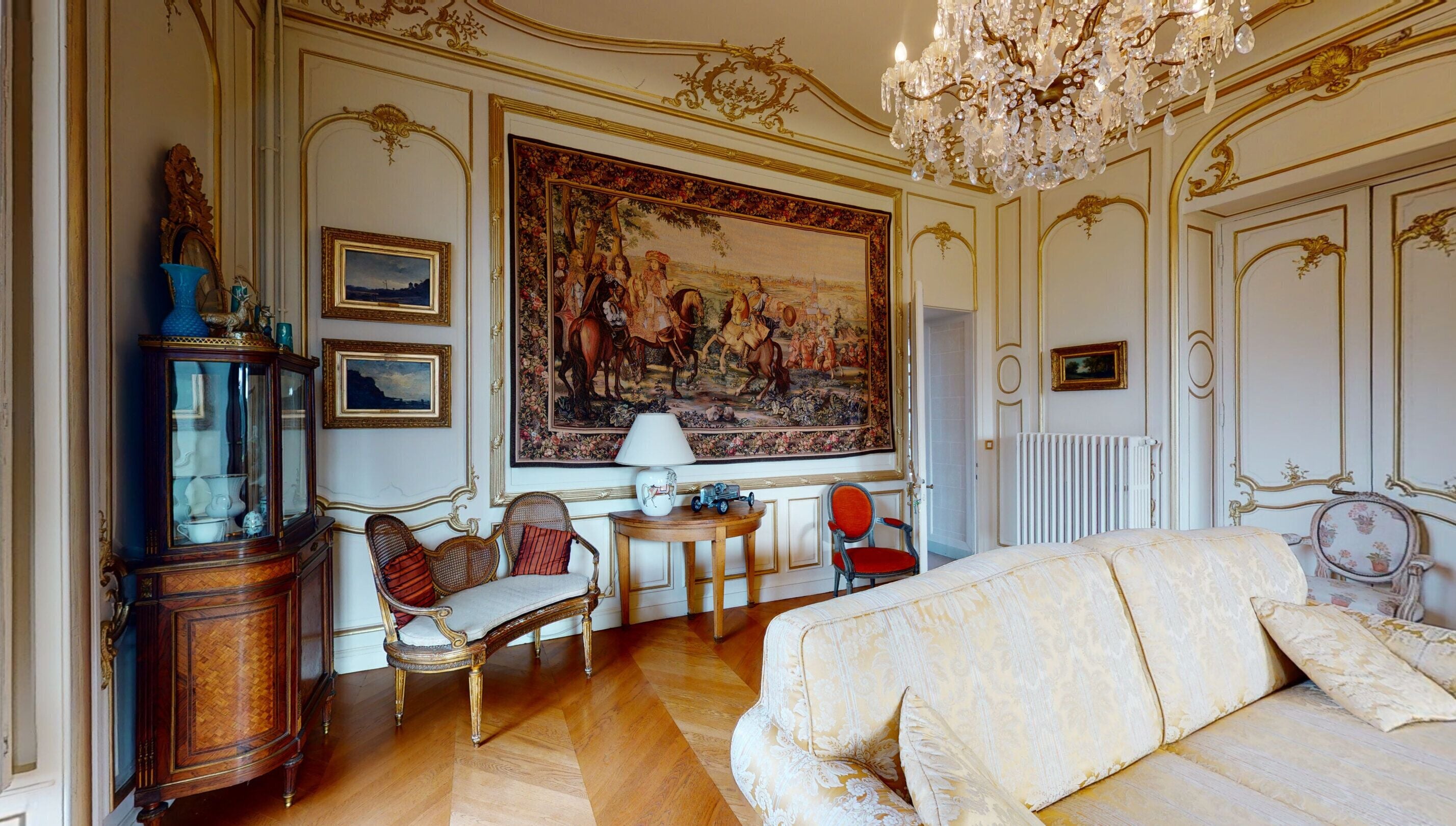 Une chambre luxueuse avec un grand lit, des meubles richement décorés, un lustre et un grand tableau au mur.