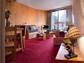 Ein gemütliches Wohnzimmer mit einer Holzdavonia, einem Fernseher, einem Esstisch und einem großen Fenster mit Vorhängen.