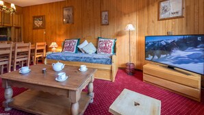 Ett mysigt rum med träväggar, en soffa med mönstrade kuddar, ett träbord med koppar, en tv och en lampa.