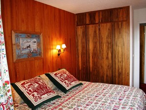 Ein Schlafzimmer mit Holzwänden, einem Bett mit floralem Bettbezug, zwei Wandlampen und einem gerahmten Bild an der Wand.