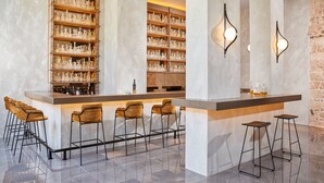 Een bar met een marmeren aanrechtblad, meerdere planken met flessen en barstoelen.