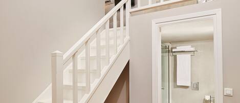 A staircase leading to a second floor with a white railing, a wooden floor, and a bathroom visible through an open door.
