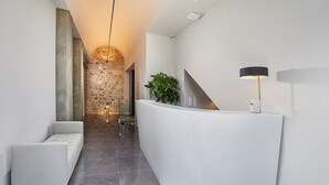 Een moderne receptiebalie met een gebogen vorm, een zithoek met een comfortabele bank, een kamerplant en een lamp.