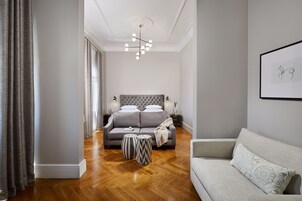 Un dormitorio moderno con un sofá gris, un cabecero capitonado y una araña.