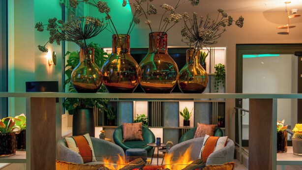 A modern living room with a fireplace, green sofas, and decorative vases. - Leonardo Royal Hotel Nürnberg (Nuremberg)