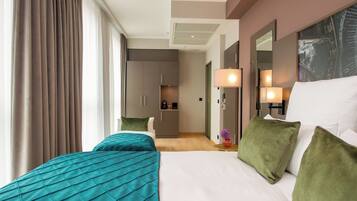 A hotel room with a large bed, a desk, and a kitchenette in the background.