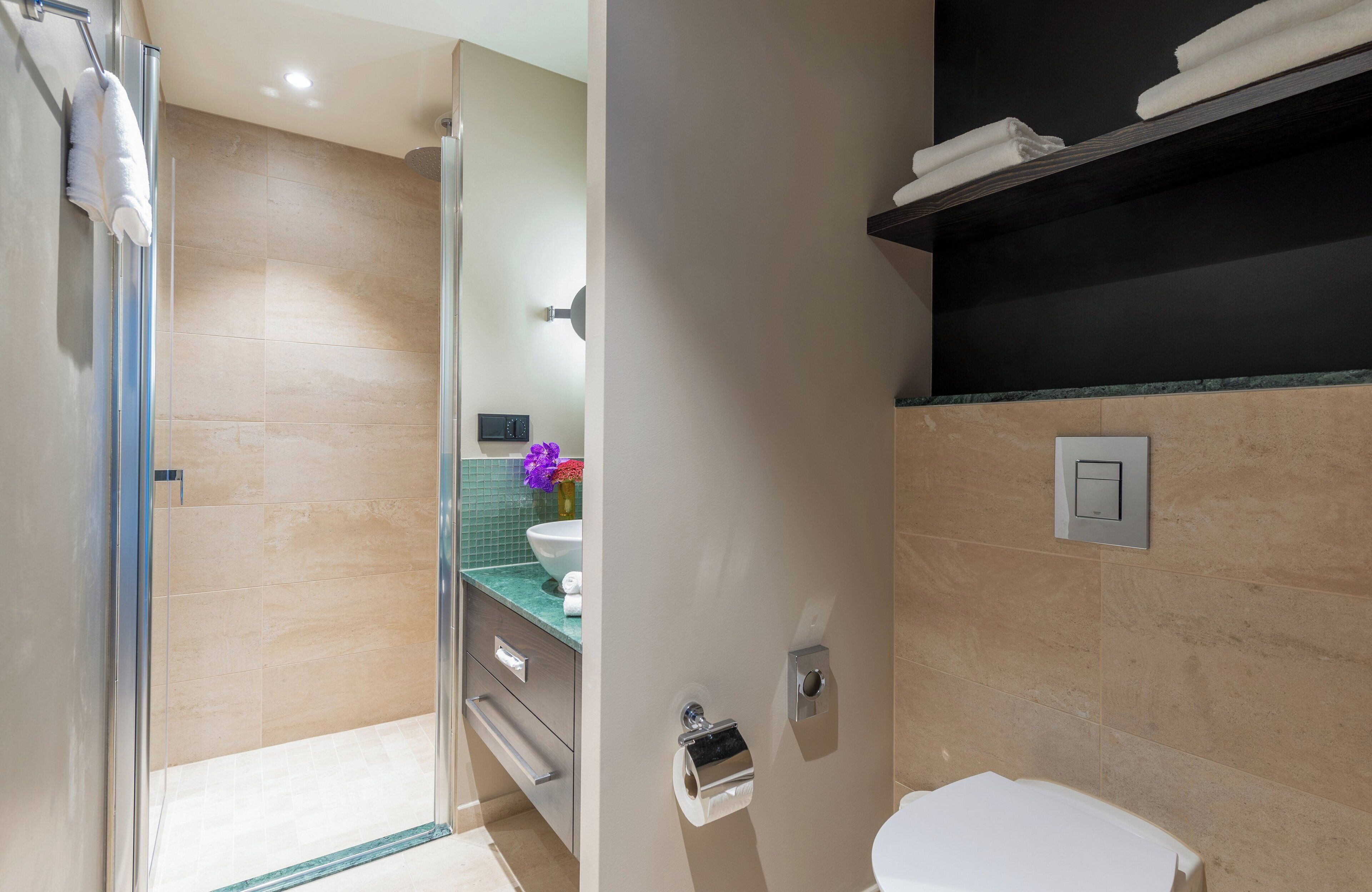 Un baño moderno con cabina de ducha de vidrio, inodoro blanco, tocador con espejo y barra para toallas.