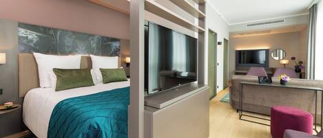 A modern hotel room with a bed, a TV, a sofa, and a small table with a lamp and flowers.