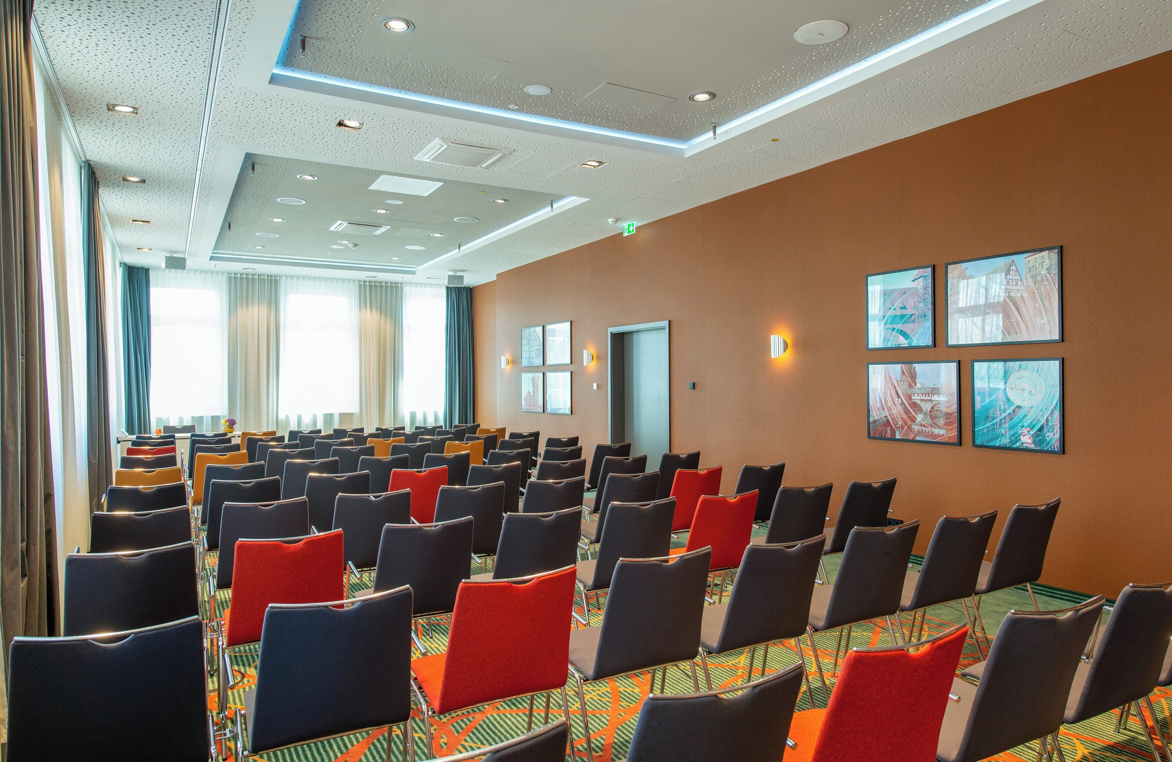 A conference room with rows of chairs, a patterned carpet, and framed artwork on the walls.