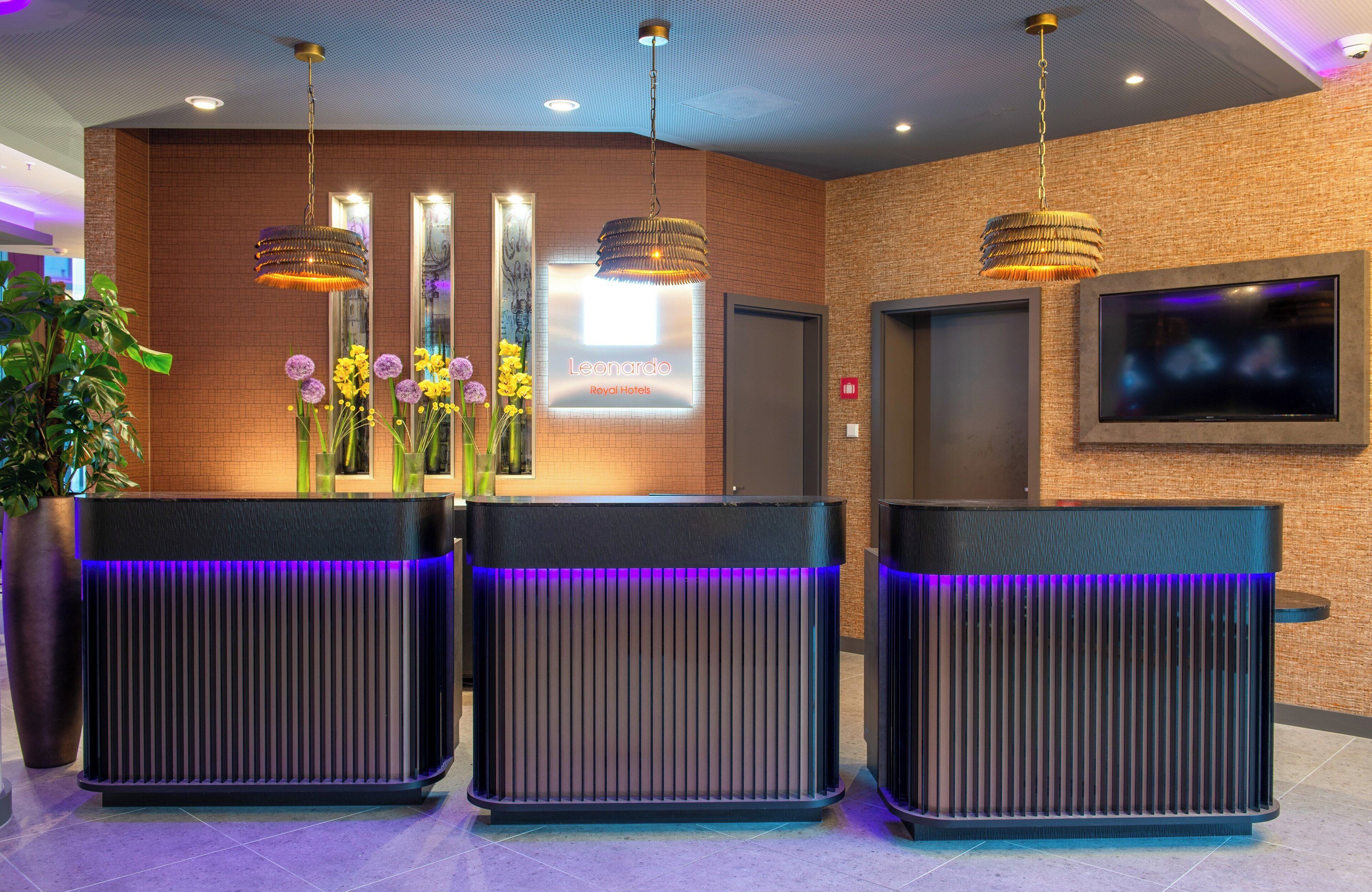 A reception area with a modern design, featuring a reception desk, a digital display, and a television screen.