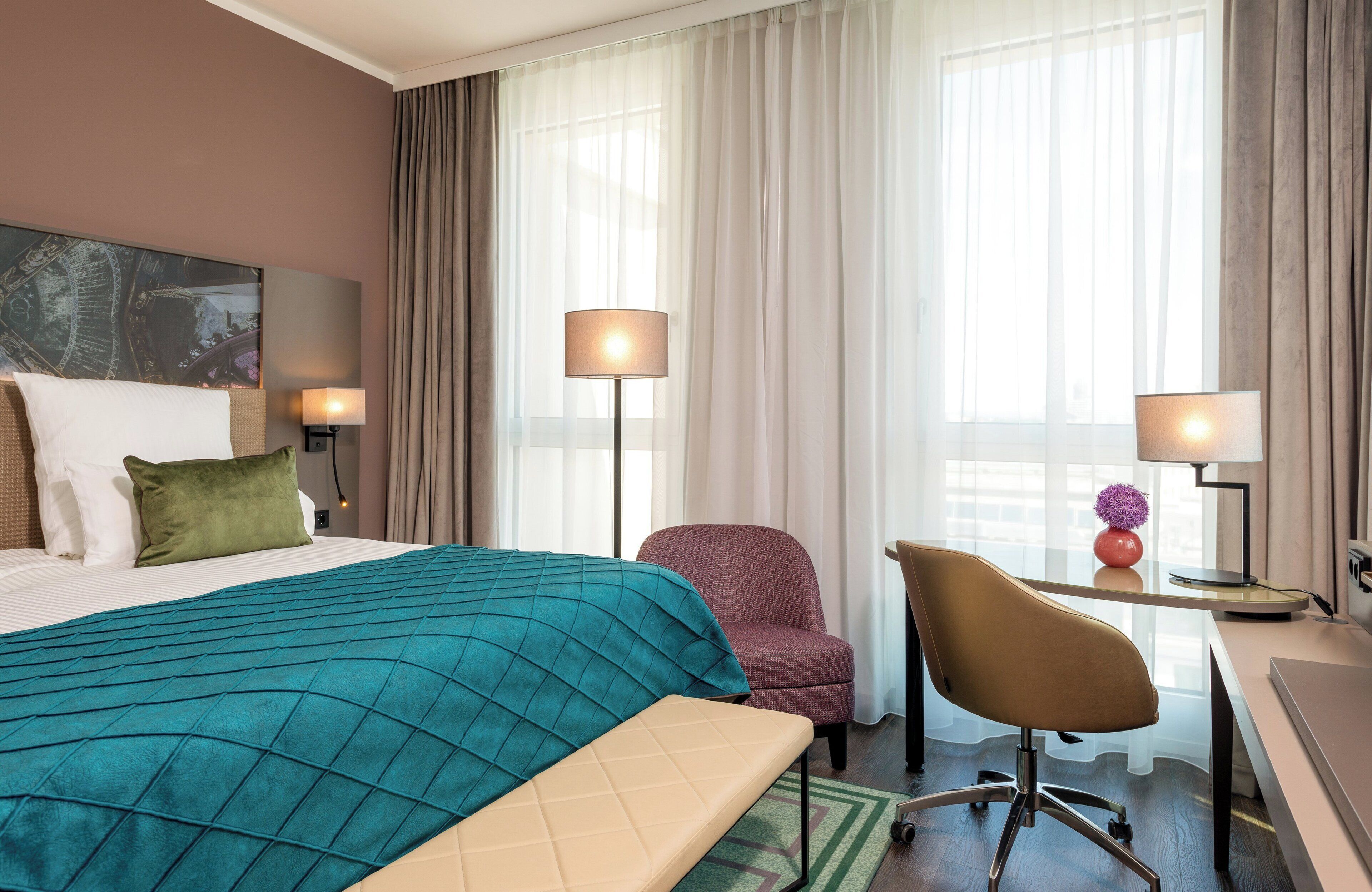 A hotel room with a bed, a desk, a chair, and a lamp.
