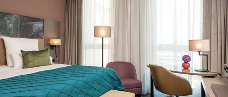 A hotel room with a bed, a desk, a chair, and a lamp.