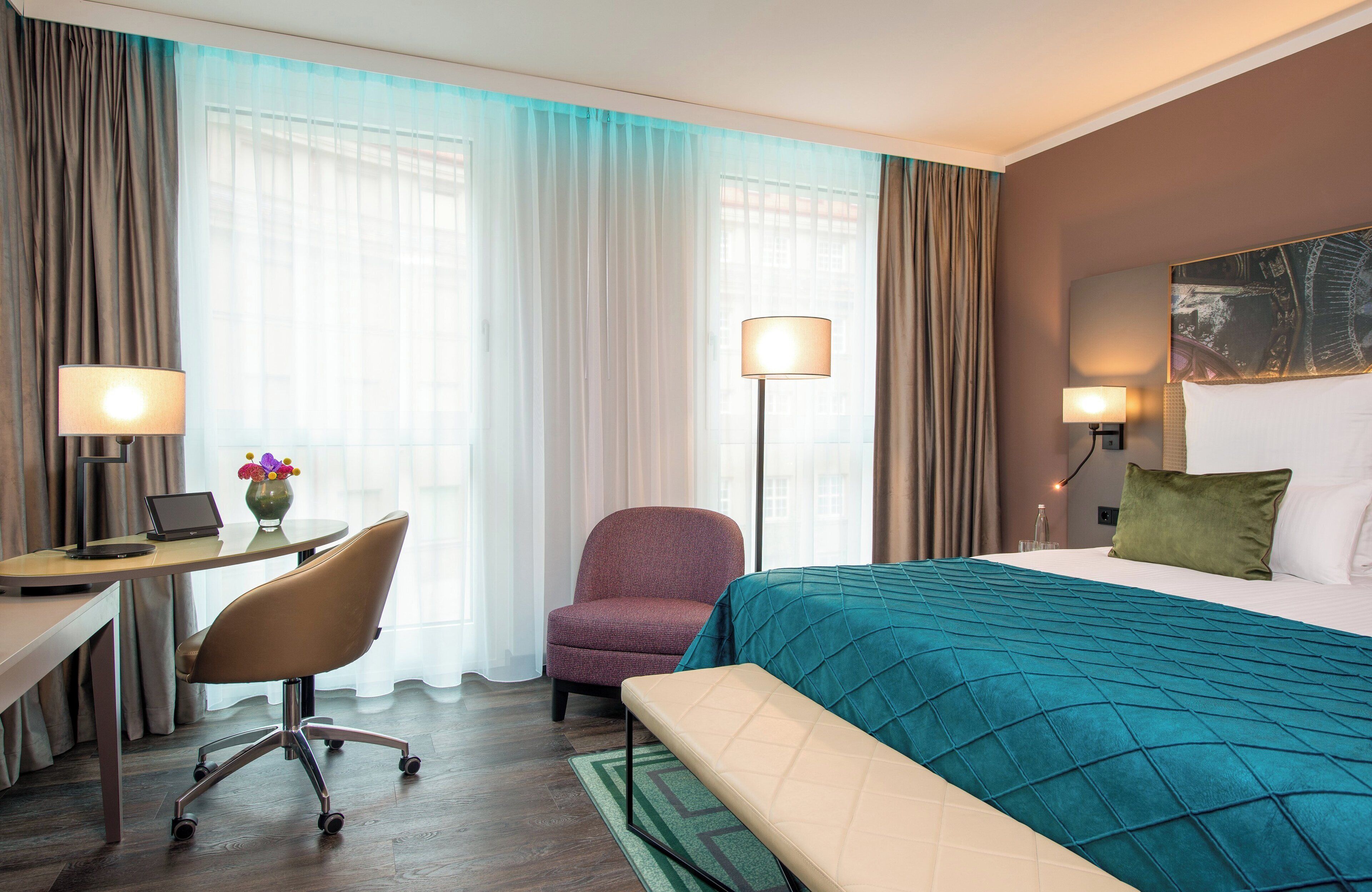 A hotel room with a bed, desk, chair, and two lamps.