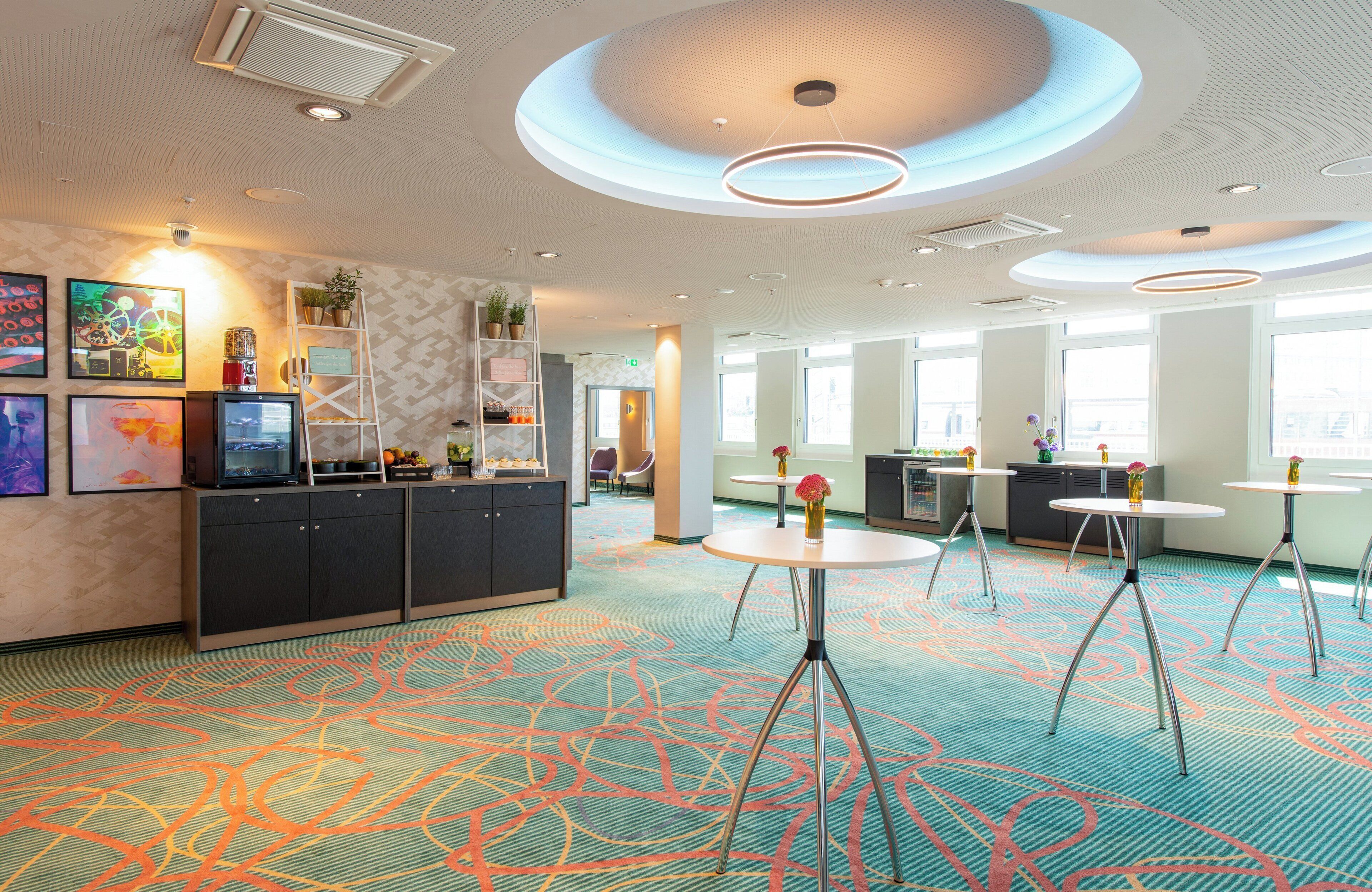 Eine moderne Hotelhalle mit einer zentralen Rezeption, mehreren Sitzbereichen und einem gemusterten Teppich.