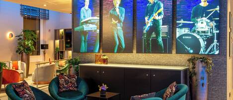 A modern lobby with teal armchairs, a reception desk, and a large wall-mounted screen displaying a band performing.