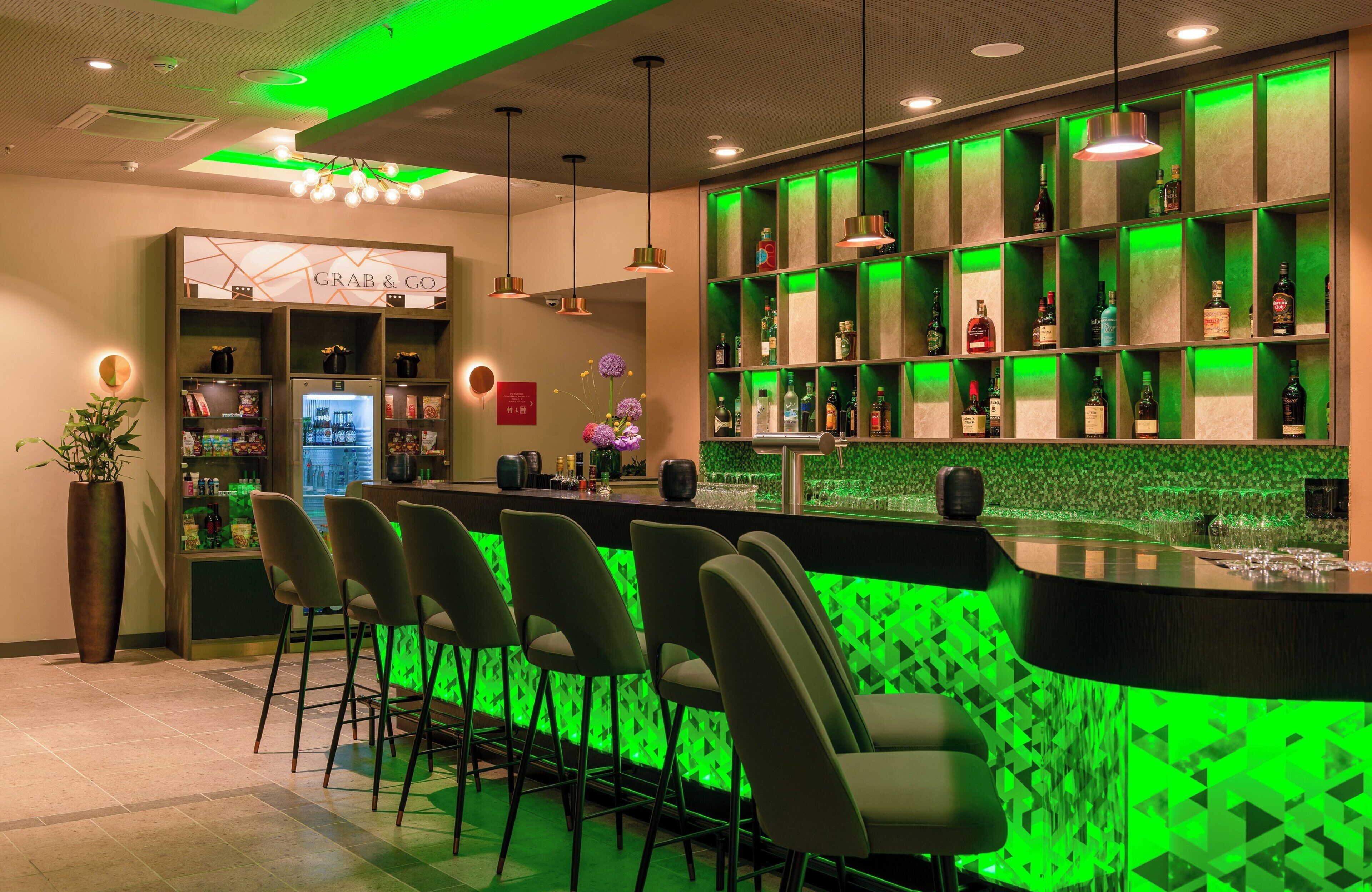 A bar area with green lighting, a 'Grab & Go' section, and a variety of bottles on shelves.