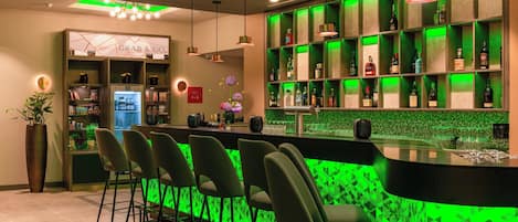 Zona de bar con iluminación verde, un espacio para 'Grab & Go' y una variedad de botellas en estanterías.