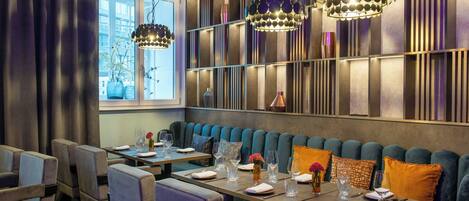 A restaurant with a long counter, blue upholstered seating, and pendant lighting.