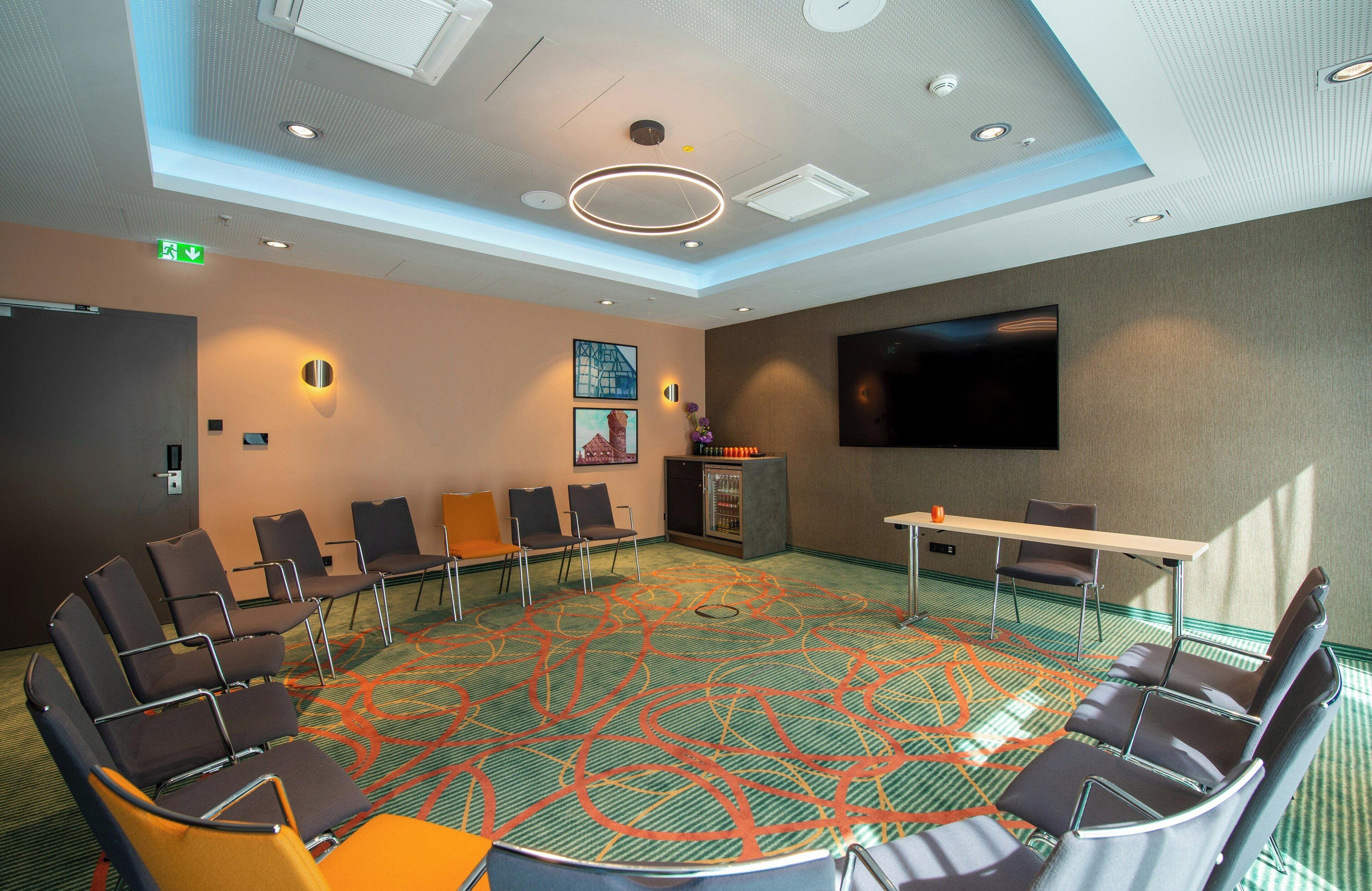 A conference room with a circular seating arrangement, a flat-screen TV, and a carpeted floor.